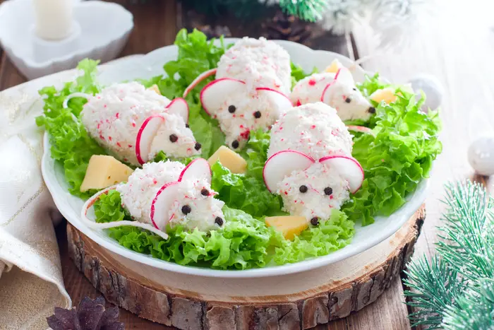 A photo of a "Celebratory Christmas crab salad in the form of mice on a dish with pieces of cheese"